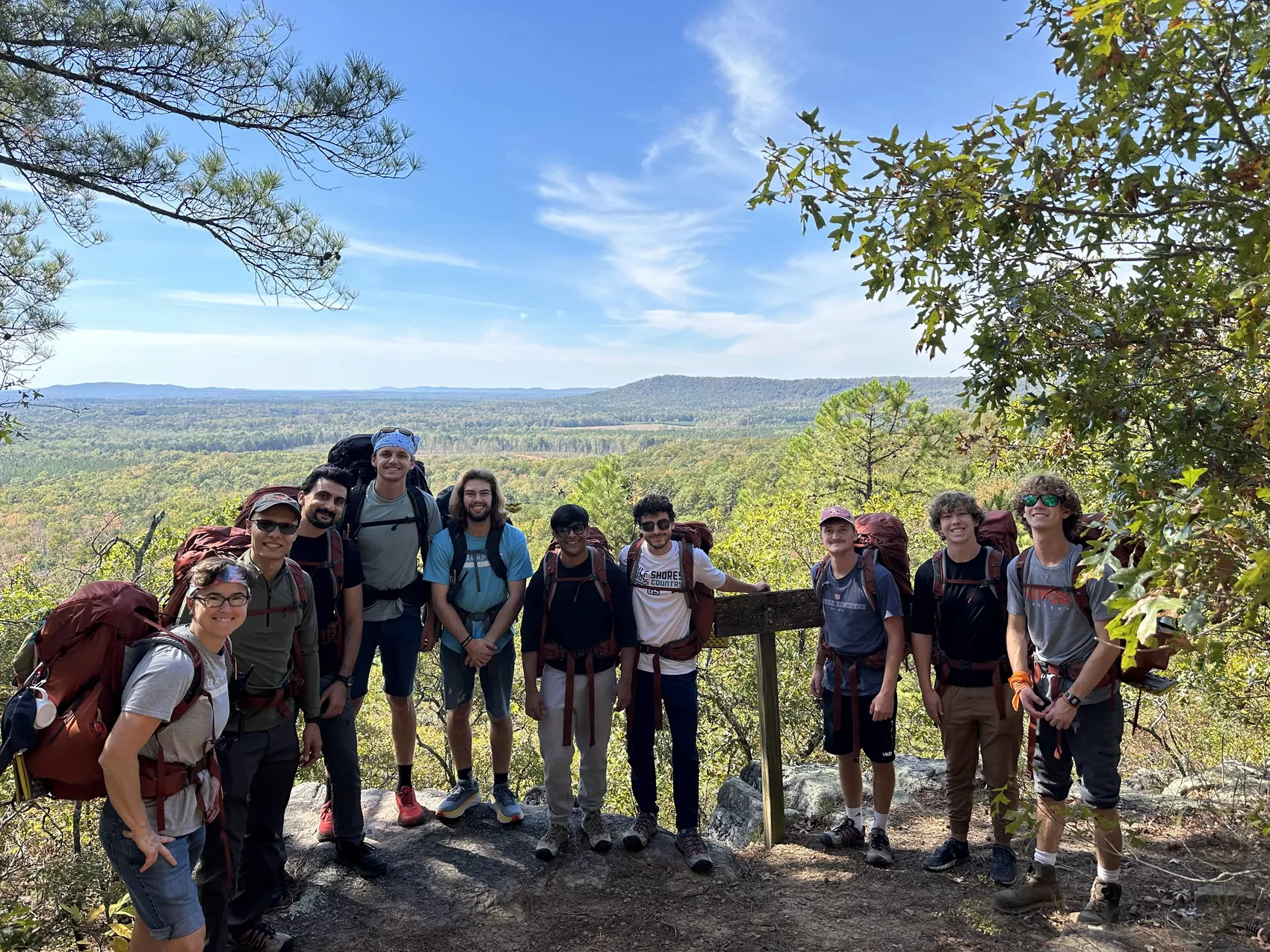A group of students stand at the top of a mountain, smiling at the camera.
