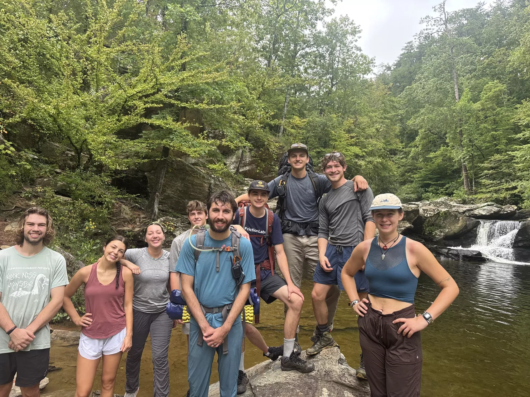 A group of students stand on a rock beside a creek, smiling.